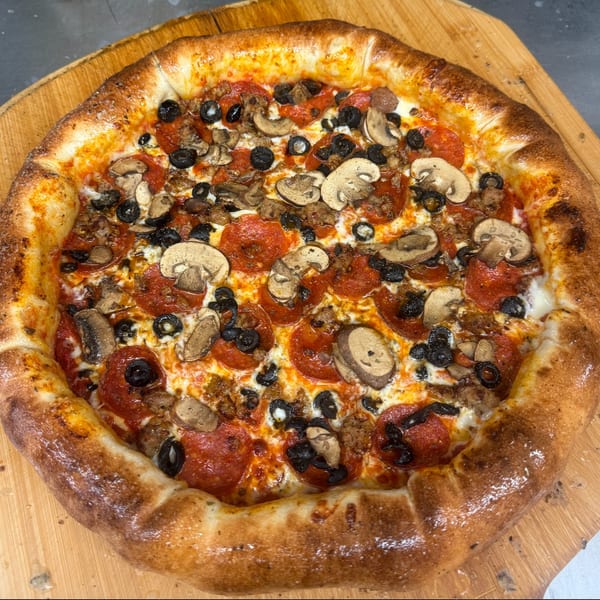 A Heavy Metal Pizza with pepperoni, sausage, mushrooms, and black olives on a wooden peel.