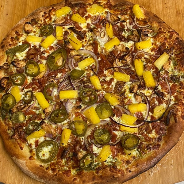 Heavy Metal Pizza with pineapple, jalapeños, red onion, and bacon on a wooden surface.