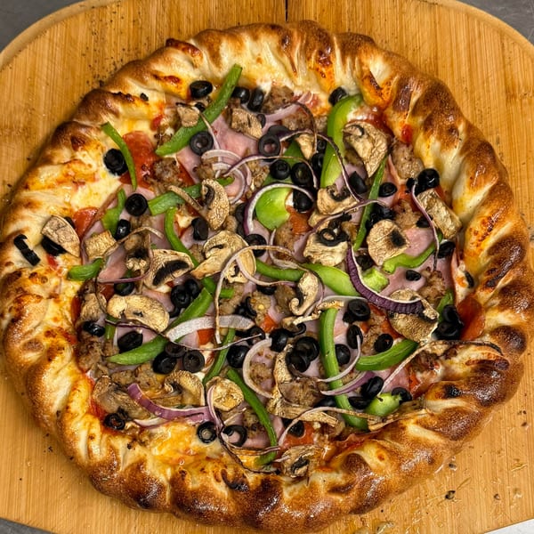 Heavy Metal Pizza's loaded pizza with mushrooms, olives, peppers, onions, and meats on a wooden board.