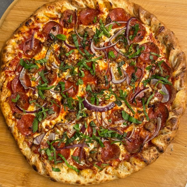 Heavy Metal Pizza's pepperoni, sausage, red onion, and basil pizza on a wooden board.