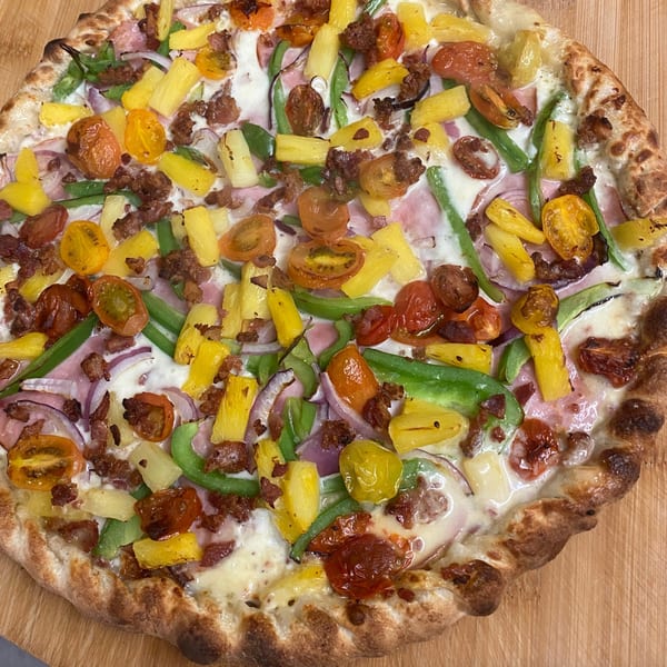 Heavy Metal Pizza with pineapple, tomatoes, green peppers, red onion, and sausage on a white sauce.