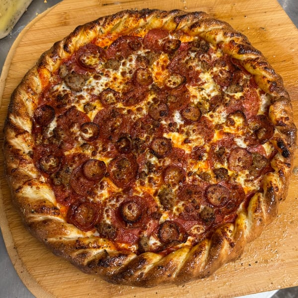 A Heavy Metal Pizza with pepperoni, sausage, and a braided crust on a wooden peel.