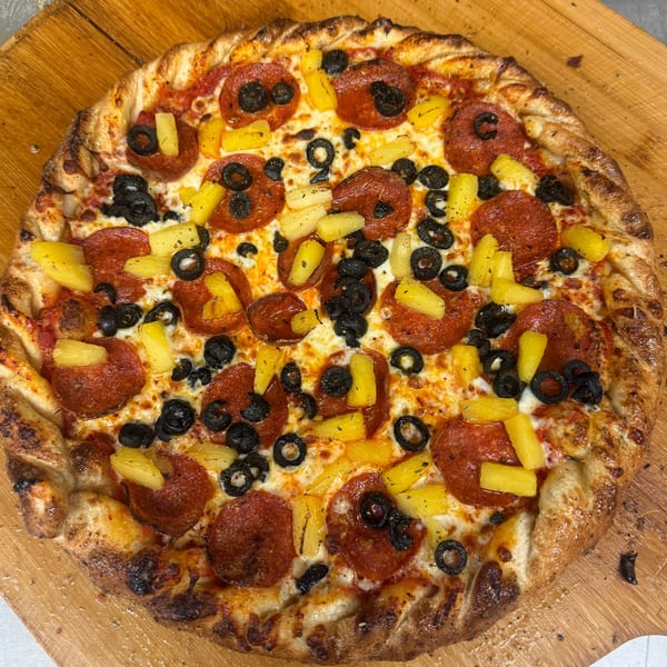Heavy Metal Pizza's pepperoni, black olive, and pineapple pizza on a wooden peel.