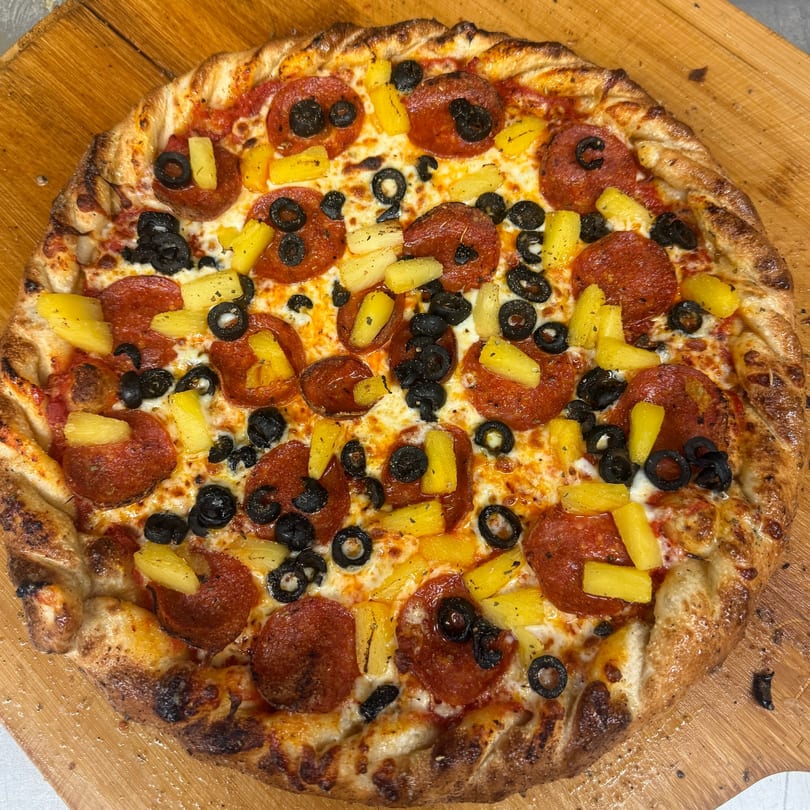 Heavy Metal Pizza's pepperoni, black olive, and pineapple pizza on a wooden peel.